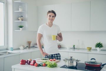 Portrait of his he nice attractive cute cheerful cheery confident guy drinking green tea making dinner lunch at light white modern style interior hotel indoors