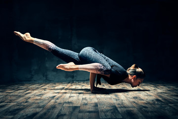 Young woman practicing yoga doing hurdler pose in dark room - obrazy, fototapety, plakaty