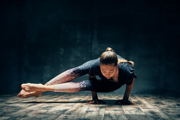 Young woman practicing yoga doing eight-angle pose asana in dark room