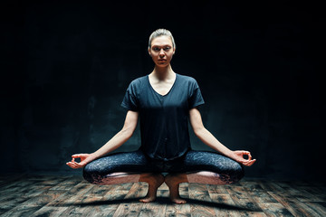 Young beautiful woman doing yoga asana tiptoe pose prapadasana variation on dark room