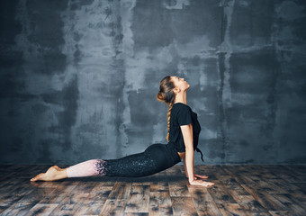 Fototapeta premium Young woman practicing yoga, doing cobra Pose on dark background