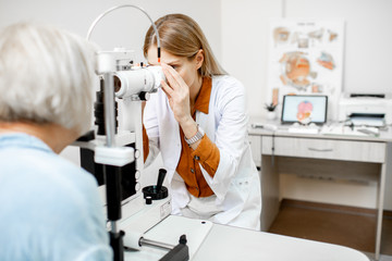 Ophthalmologist examining eyes of a senior patient using microscope during a medical examination in the ophthalmologic office - obrazy, fototapety, plakaty