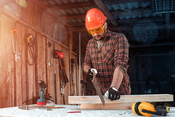 A man carpenter cuts a wooden beam using a handsaw, male hands with a saw closeup. Work with wood.