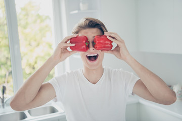Close-up portrait of his he nice attractive cheerful glad cheery comic childish funky guy closing eyes with fresh red pepper at light white modern style interior hotel indoors
