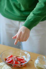 girl pours sesame seeds into a salad with tomatoes