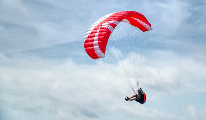 Fototapeta na wymiar Paraglider in action in cloudy skies with red parachute