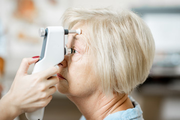 Doctor measuring the eye pressure with modern tonometer to a senior patient in the medical office, close-up