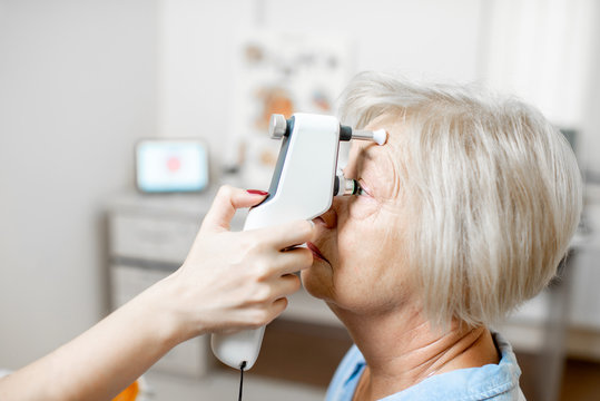 Doctor measuring the eye pressure with modern tonometer to a senior patient in the medical office, close-up