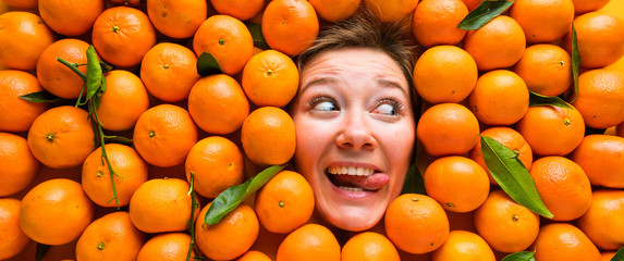 Face of laughing young woman in orange plane. Creative background with mandarins