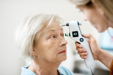 Female ophthalmologist measuring the eye pressure with modern tonometer to a senior patient in the...