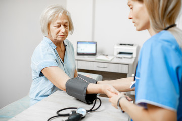 Nurse measuring blood pressure of a senior woman patient with tonometr during an examination in the clinic. Senior care concept