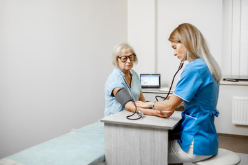 Nurse measuring blood pressure of a senior woman patient during an examination in the clinic....