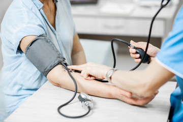 Nurse measuring blood pressure of a senior woman patient during an examination in the clinic,...
