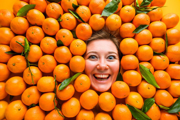 Face of laughing young woman in orange plane. Creative background with mandarins