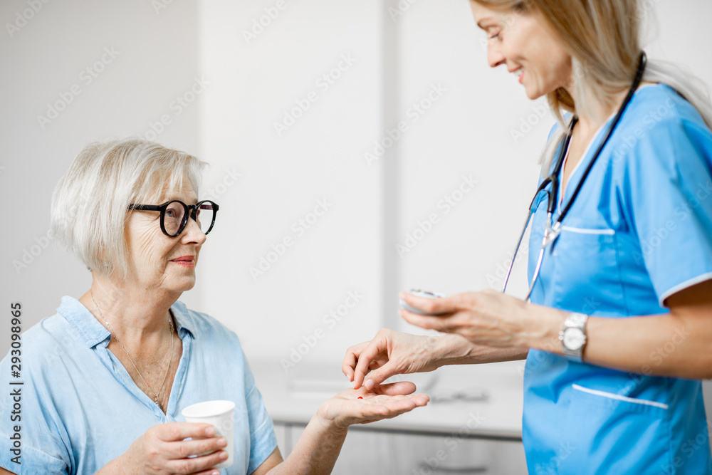 Wall mural nurse giving some medicine for a senior woman sitting on the couch, taking care of elder patients in