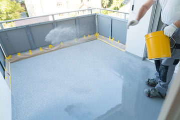 construction worker renovates balcony floor and spreads chip floor covering on resin and glue coating before applying water sealant - obrazy, fototapety, plakaty
