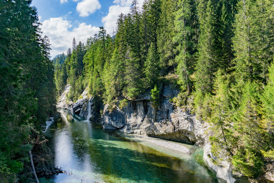 idyllic landscape with a mountain lake and small waterfall surrounded by green coniferous forest