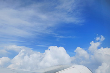 Beautiful view from airplane's window with airplane's wing, blue sky and white cloud in the summer morning. Soft focus. Transportation and nature concept.