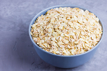 Dry oatmeal in bowl. Oat flakes on cement background. Cereals for making healthy breakfast