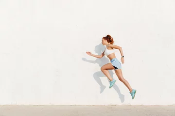 Foto op Plexiglas Image of redhead young woman running along white wall while doing workout in morning © Drobot Dean