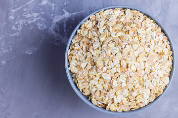 Dry oatmeal in bowl. Oat flakes on cement background. Cereals for making healthy breakfast