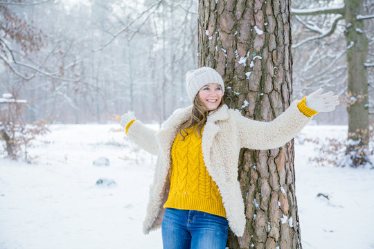sch&ouml;ne gl&uuml;ckliche junge Frau, die am Baum im Winterwald sich lehnt