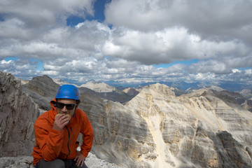 young male mountain climber on a Dolomite mountain peak enjoying the view and eating a sandwich