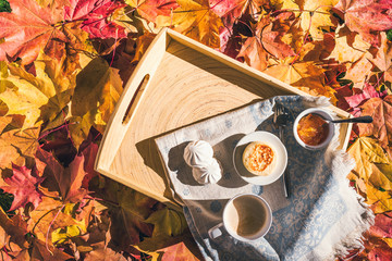 Morning breakfast. cup of coffee, marshmallow jam and a cottage cheese pancake on a wooden tray. Autumn garden with colorful maple leaves. Golden sunny autumn. Aerial view