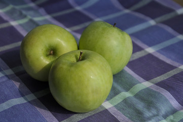 Still life with three ripe green apples on napkin