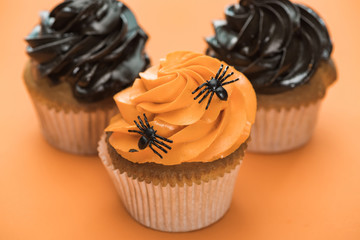 selective focus of delicious Halloween cupcakes with spiders on orange background