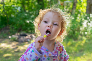 Little girl brushes her teeth on the nature in the country, sunny summer day. Oral hygiene concept.