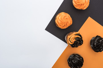 top view of delicious Halloween cupcakes on black, orange and white background with copy space