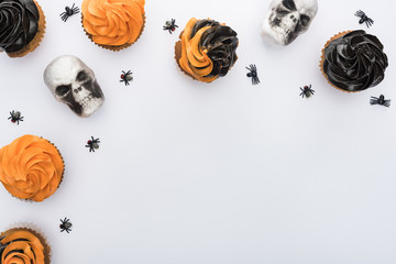top view of Halloween cupcakes with spiders and skulls on white background with copy space