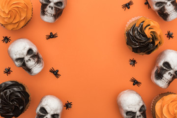 top view of tasty Halloween cupcakes with spiders and skulls on orange background with copy space