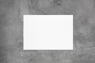 Empty white horizontal rectangle poster or card mockup with soft shadow on dark grey concrete wall background. Flat lay, top view