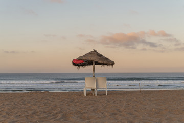 Sunrise on an empty beach with an sun umbrella and two chairs.