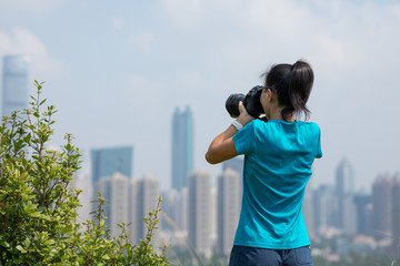Female photographer taking pictures on mountains next to modern city
