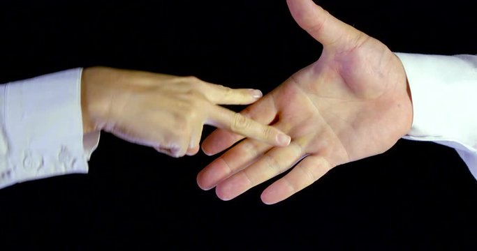 Close-up of a woman and a man's hand in white sleeves on a black background playing rock, paper, scissors. The woman's scissors fell out, the man's paper and the woman's hand won.
