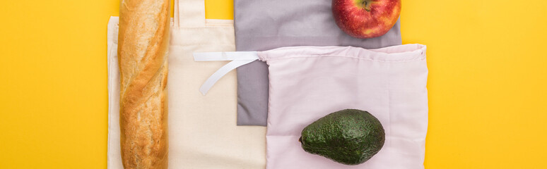 top view of apple, baguette and avocado on eco friendly bags isolated on yellow, panoramic shot