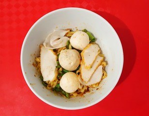 A bowl of yellow noodles with many kind of fish ball on top view.