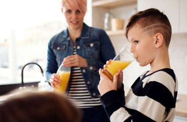 A young woman with children drinking juice in a kitchen.