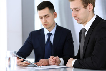 Businessmen or partners working together while using tablet computer at the desk in modern office. Headshot of male entrepreneur or manager with colleague at workplace. Teamwork, partnership and