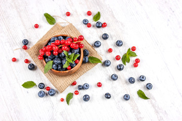 Fresh blueberries and red currants with mint leaves in a wooden bowl on burlap. Diet food, vegan berries