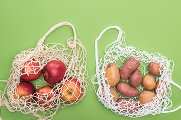 top view of ripe apples and potatoes in string bags isolated on green