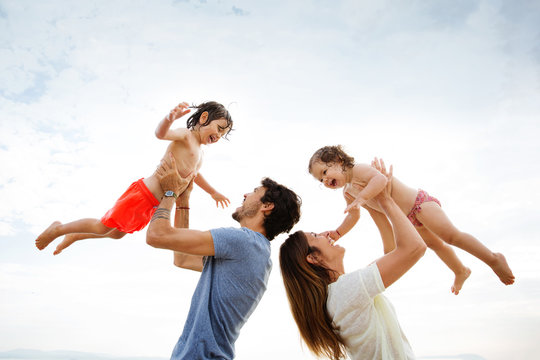 Low angle view of parents lifting children against sky at beach
