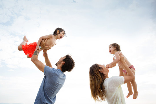 Low angle view of parents lifting children against sky