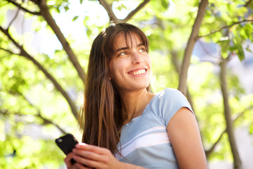 beautiful young woman with long hair smiling with cellphone in park