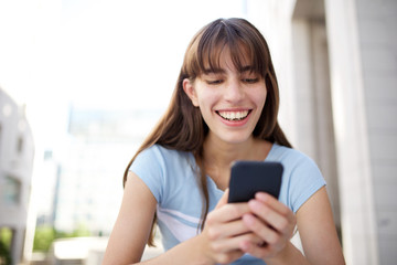 Close up beautiful smiling young woman looking at mobile phone outside