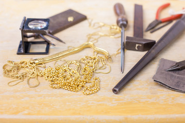 Gold accessory repair tools, broken knot of golden necklace on wooden table. Old expensive jewelry...