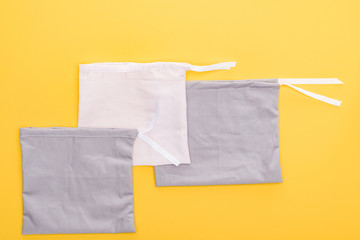 Fototapeta na wymiar top view of cotton white and grey eco friendly bags isolated on yellow